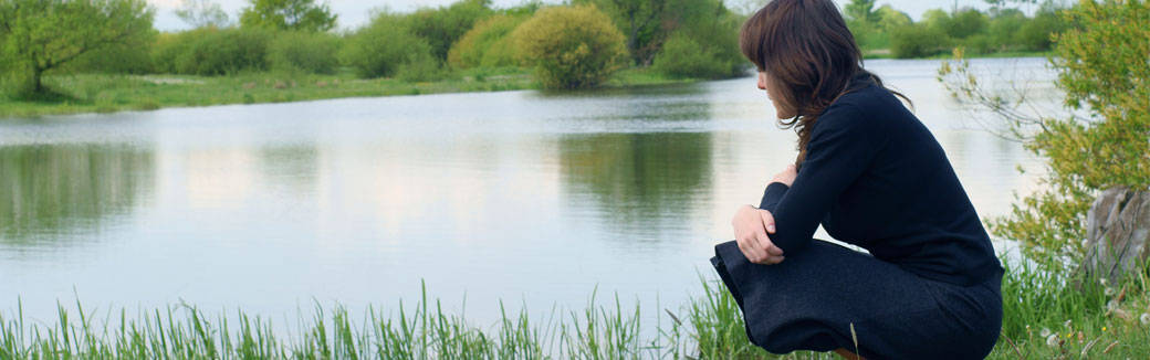 Woman sitting on the shore of a lake, gazing at water.